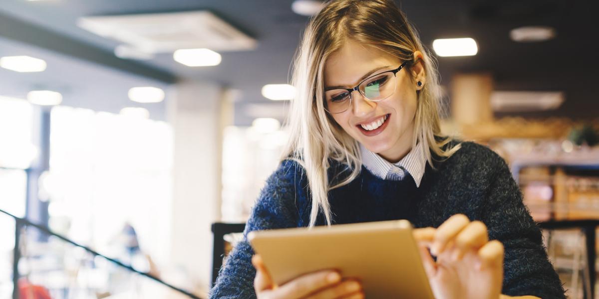 Student smiling while using a tablet in a library