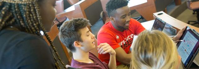 Group of students in a classroom all looking at an iPad together